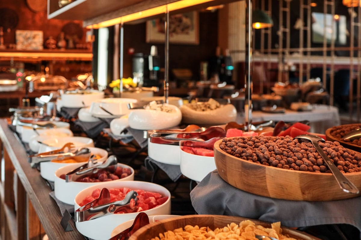 Rich hotel breakfast buffet with bowls of fresh fruits, cereals, nuts, cheeses, and cold cuts on a stylish counter with serving utensils