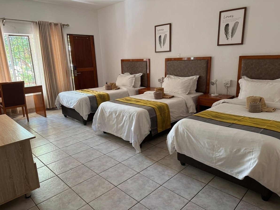 Spacious hotel room with three twin beds, white linens, wooden headboards, and olive green accent runners