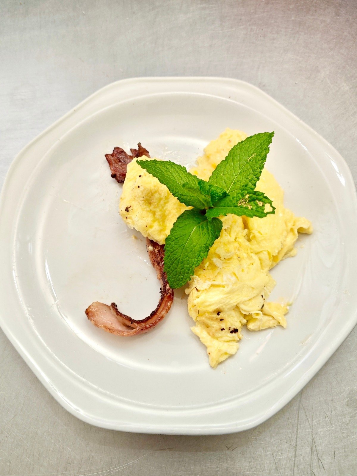 Scrambled eggs with crispy bacon and fresh mint garnish on a white plate