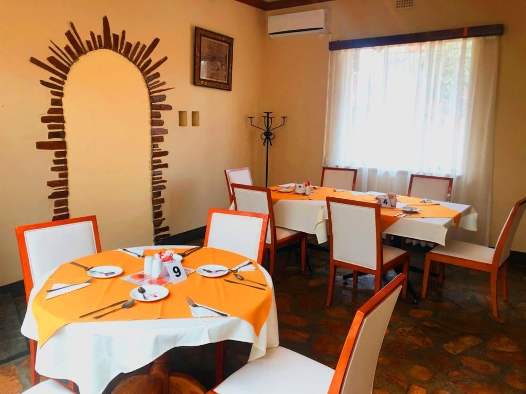 Warm-toned dining room with orange and white chairs at two round and rectangular tables, featuring decorative archway and window with natural light