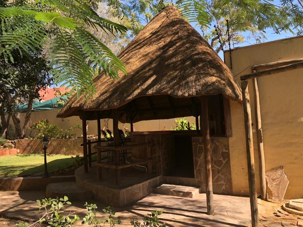 Traditional thatched-roof shelter with wooden structure in a garden setting surrounded by green vegetation and trees