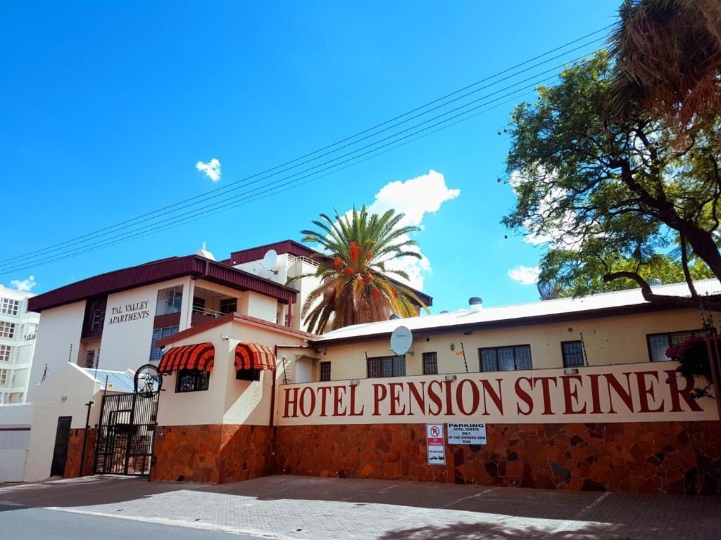 Hotel Pension Steiner building with terracotta facade, palm tree, and red signage under a clear blue sky