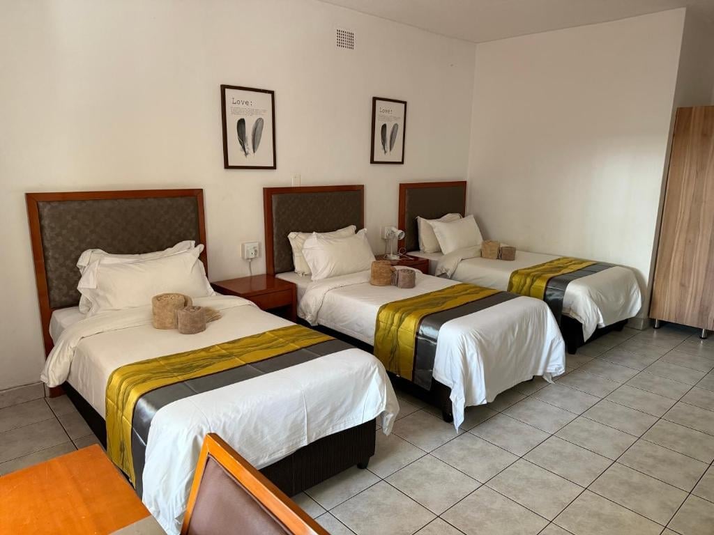 Hotel room with three twin beds, white linens, gold accent runners, wood headboards, and beige walls