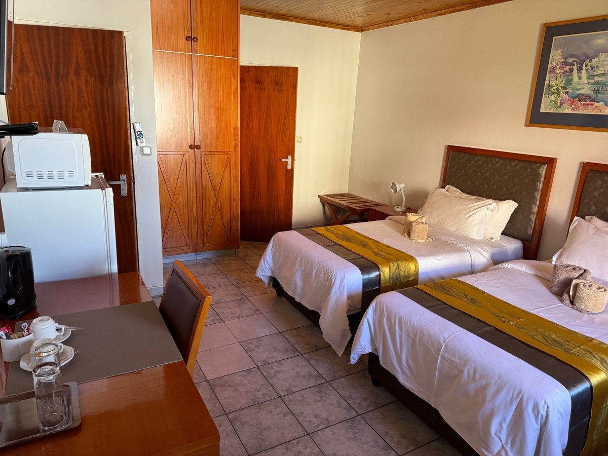 Hotel room with two twin beds, wooden wardrobe, mini refrigerator, and framed artwork on beige walls