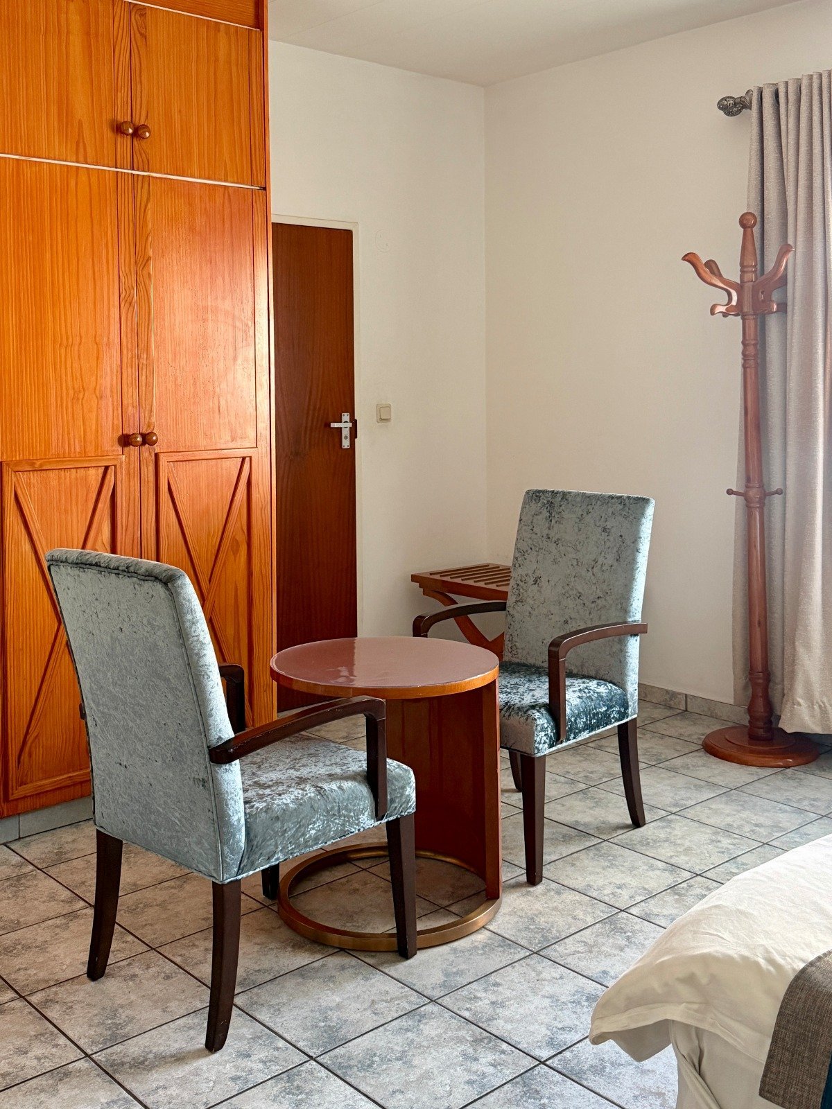 Modern living room with two upholstered chairs, round wooden table, orange wooden cabinets, and wooden coat rack