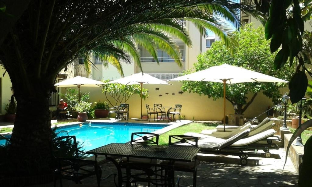 Courtyard with swimming pool, lounge chairs, white umbrellas, palm trees, and a cream-colored building