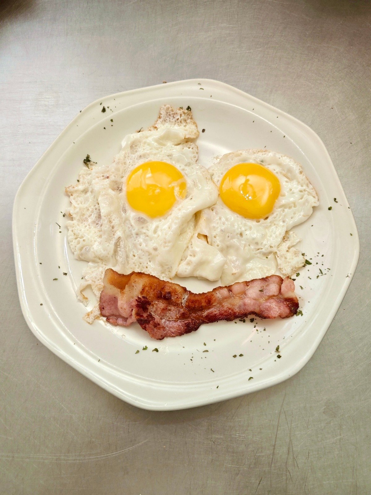 Plate of fried eggs and bacon arranged to resemble a smiling face with sunny-side-up eyes