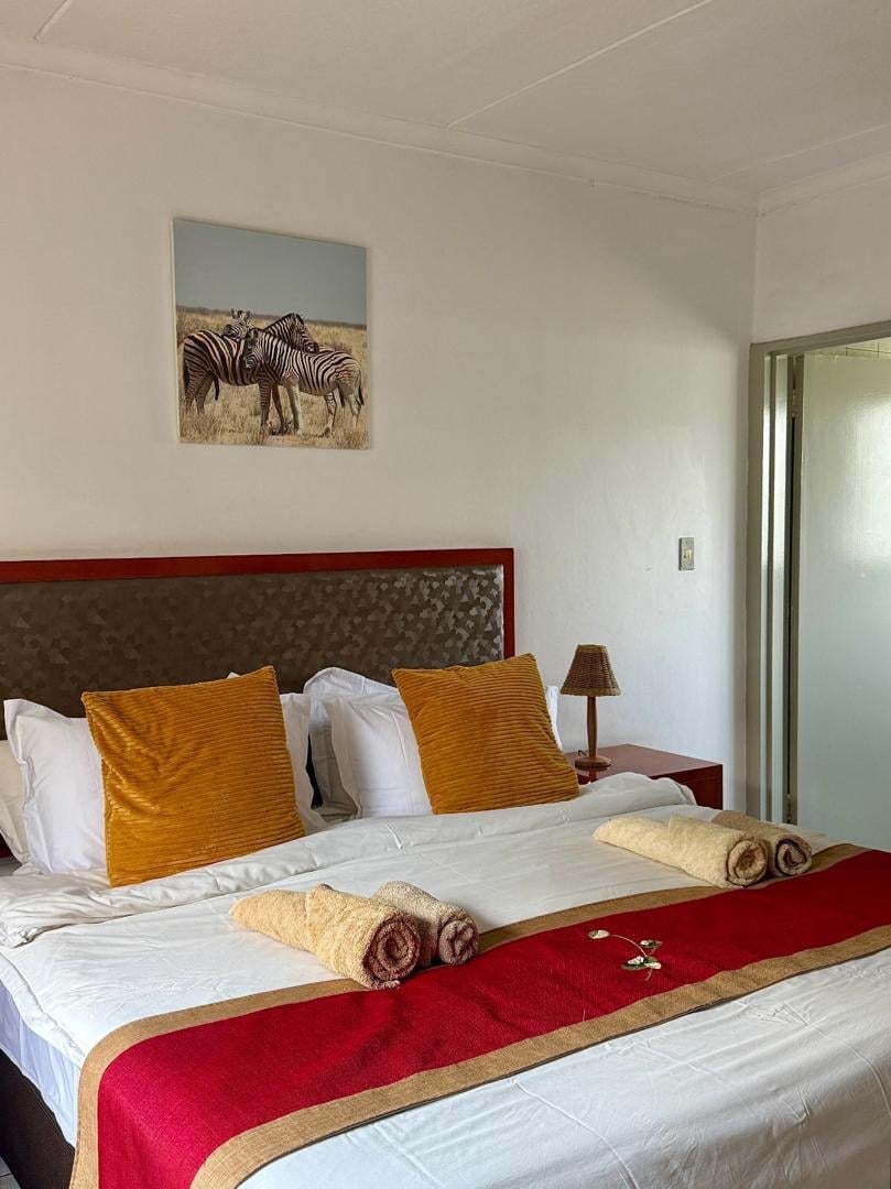 Modern bedroom with red-framed bed, white linens, gold pillows, red throw blanket with rolled towels, and zebra artwork on wall
