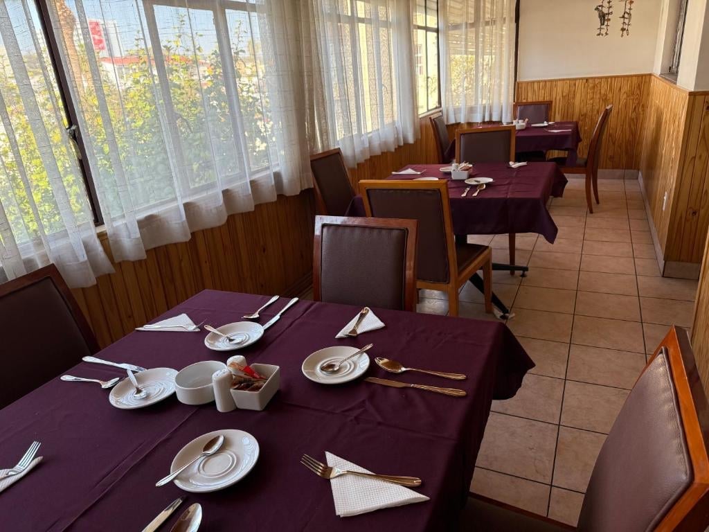 Restaurant dining room with purple tablecloths, place settings, wooden chairs, and floor-to-ceiling windows with natural light.