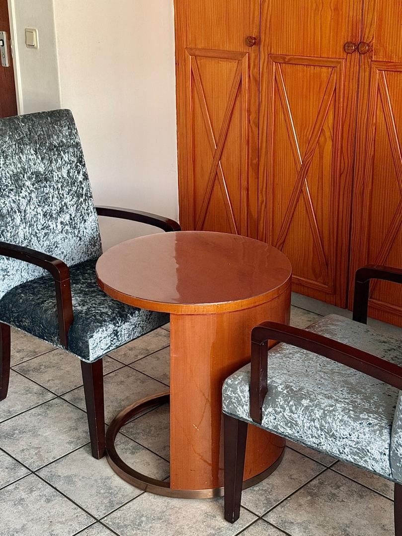 Wooden round side table with two upholstered chairs in a room with ornate wooden cabinet doors