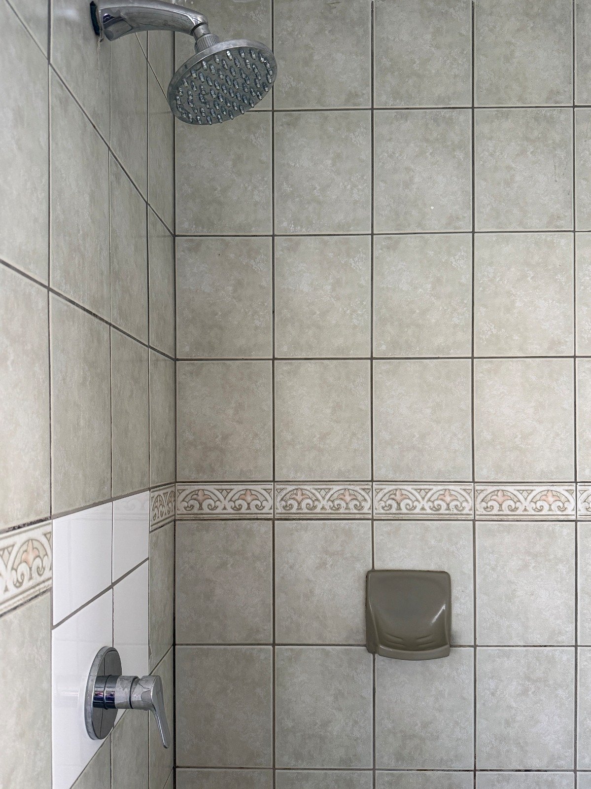 Modern shower enclosure with gray tile walls, round showerhead, chrome fixtures, soap niche, and decorative border trim