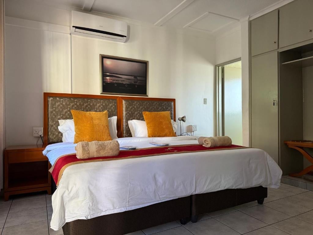 Modern bedroom with a queen bed featuring white linens, mustard yellow and patterned throw pillows, and a wooden headboard with bedside tables