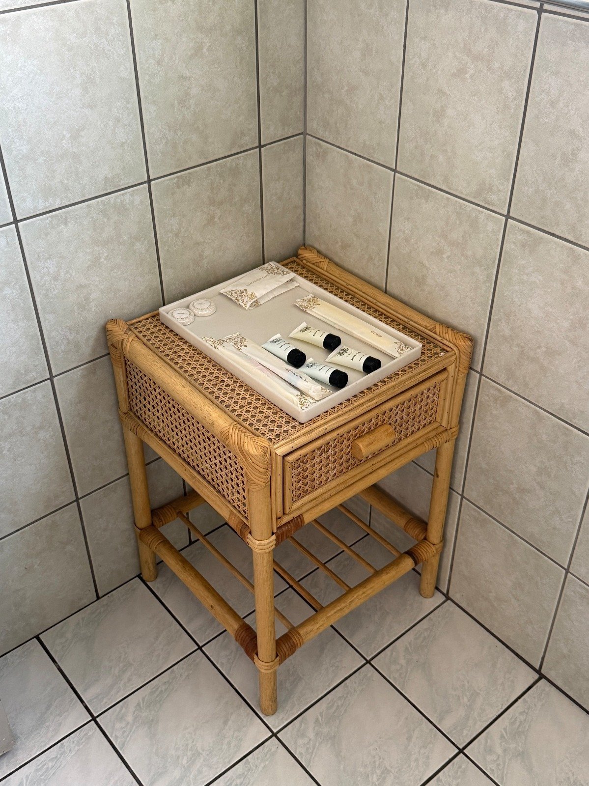 Wooden rattan nightstand with light switch outlet cover in corner of tiled bathroom