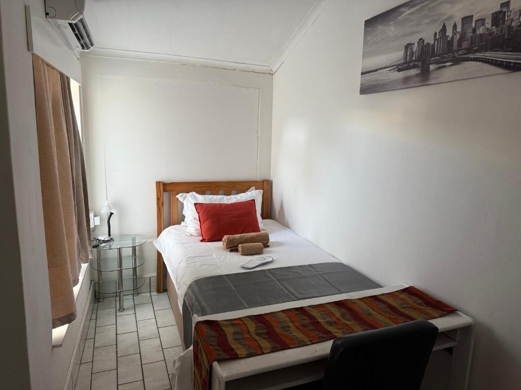 Small minimalist bedroom with single bed, white bedding, red pillow, and cityscape poster on wall