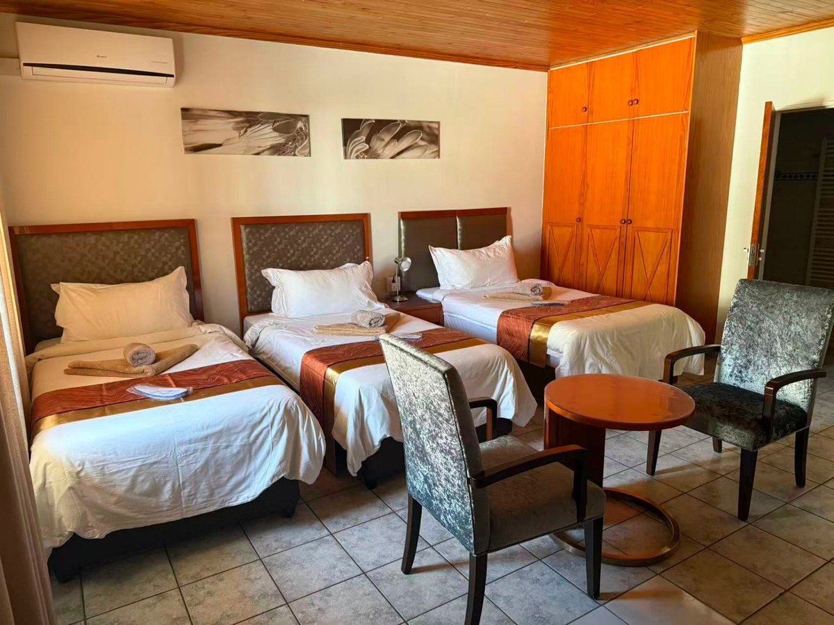 Hotel room with three twin beds, wooden furniture, orange wardrobe, and beige walls with artwork